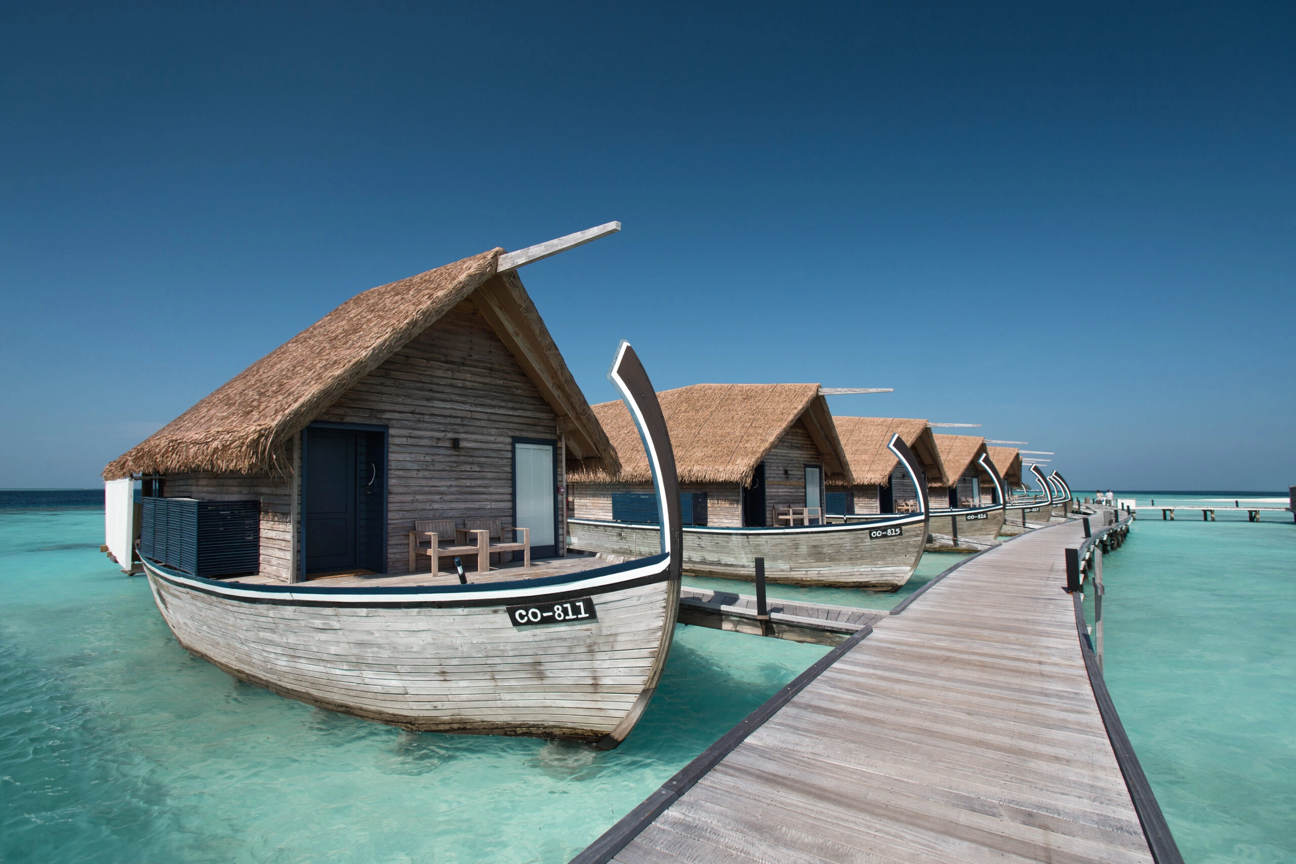 Overwater villa with thatched roof and traditional Dhoni boat on a wooden jetty in the Maldives
